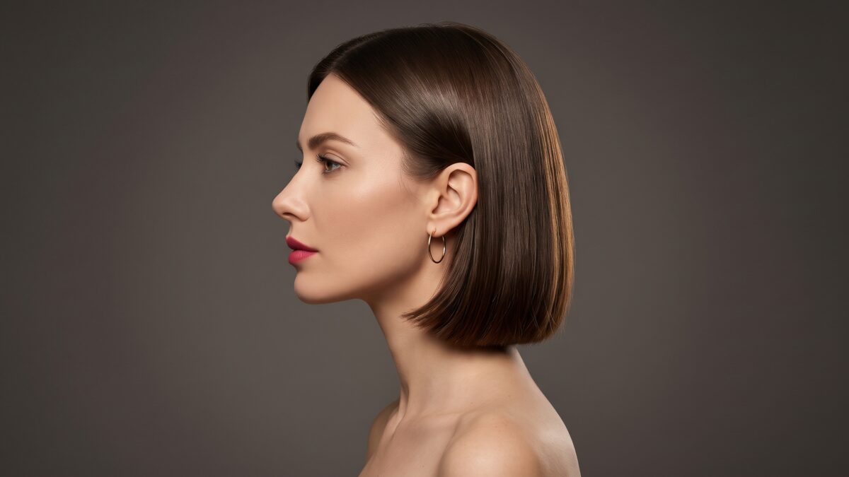 Perfil de mujer con bob clásico castaño chocolate de corte recto y brillo espejo sobre fondo gris carbón